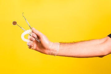 Dentist hand shows and holds mirror, scaler and a dental aligner, isolated on yellow background.