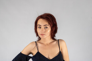 A young female attractive caucasian model with album red hair in a studio with a white background wearing a black dress.