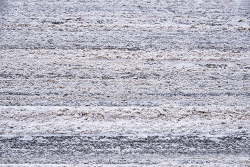 Dirty snow slush, salt and melting reagents on the road with traces from cars. Snow and slush covered highway after huge snowfall, dangerous driving conditions. Road under the snow, slippery