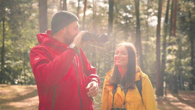 Young girl approaches to Caucasian man with binoculars in woods, and takes photo on camera seeing beautiful view.