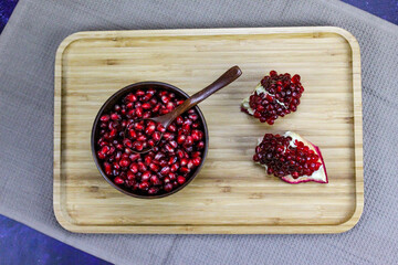 Red pomegranate seeds close up in a wooden bowl with a wooden spoon. Two pieces of pomegranate with ripe red seeds on a wooden tray.
