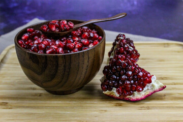 Red pomegranate seeds close up in a wooden bowl with a wooden spoon. Two pieces of pomegranate with ripe red seeds on a wooden tray.