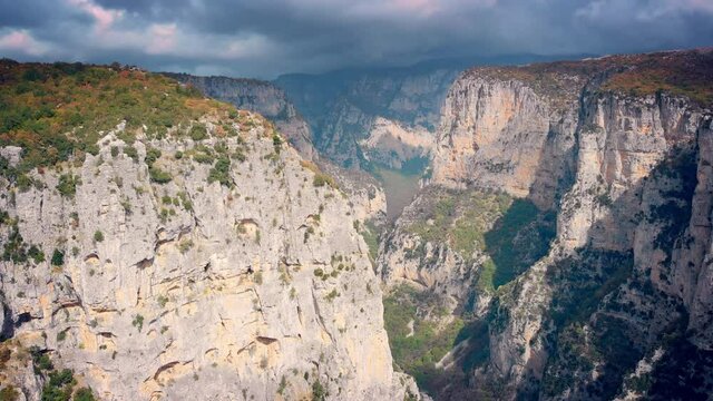 Aerial forward motion over Vikos Gorge beautiful landscape, rocky canyon steep slopes, green trees and dramatic sky