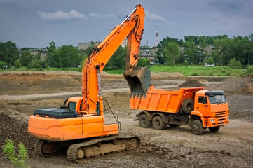 Orange excavator and orange dump truck at a construction site.