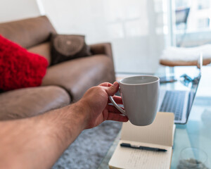 Hispanic arm handing a cup of coffee on his workplace at his home