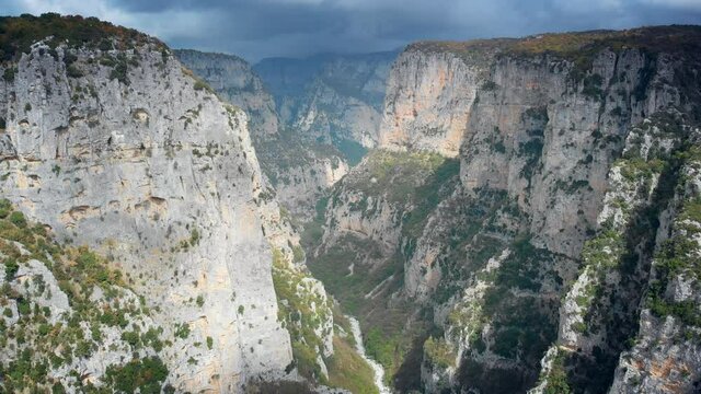 Lateral aerial motion view on Vikos Gorge dramatic nature, rocky canyon steep slopes with green vegetation, cloudy sky