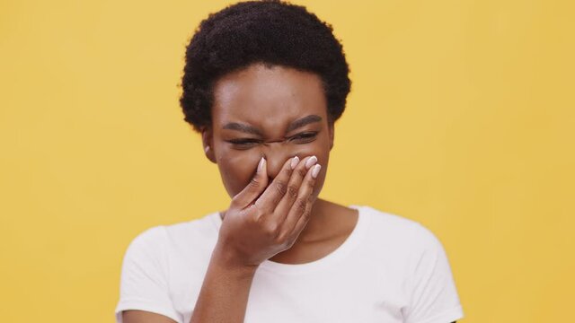 Close up portrait of young displeased african american woman smelling stinky odor, closing her nose, orange background