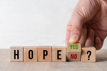 hand turning a cube with text YES and NO answering the question HOPE? on wooden background