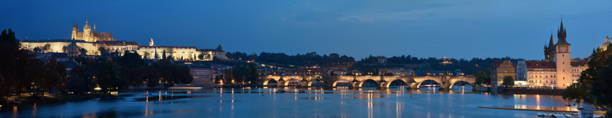 Prague riverside at night. Panoramic image of illuminated Charles Bridge and Novotnevo Lavka riverside buildings with a clock tower