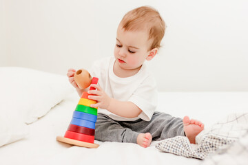 Cute baby boy playing colorful pyramid tower on white bed
