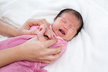 crying newborn baby wrap in blanket and parent hands on bed