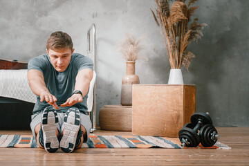 A young man goes in for sports at home, online workout from the phone. The athlete  stretching  in the bedroom, in the background there is a bed, a carpet.