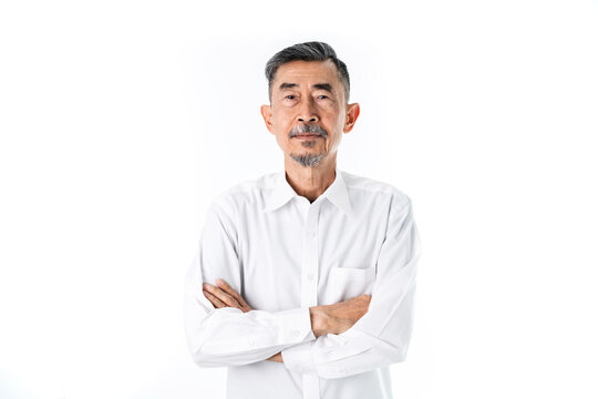 An Old Asian Man Wearing A White Shirt Is Happy And Proud. He Has Crossed His Arms With Two Hands. Studio Shot Over White Background. Elderly And Happy Positive Single Senior Retired Concept