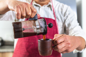 Close-up of male hands a man whose face is not seen serving fresh coffee from a French press into a mug