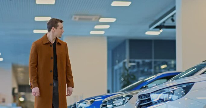 Young male businessman walks through a car dealership and looks at new models of cars. Man wants to make a car purchase, car business. 4k, ProRes