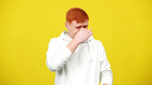 Young man closing nose smelling unpleasant smell. Middle shot portrait of Caucasian millennial guy at yellow background. Disgust concept.