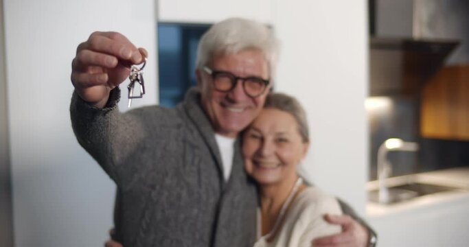 Senior man holding keys and embracing wife in new house