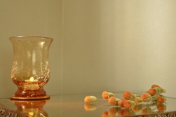 globe amaranth.  dried flower with  “art deco” crystal vase candle.  This antique mahogany side table is made in England. dim lighting  room soft focus image.