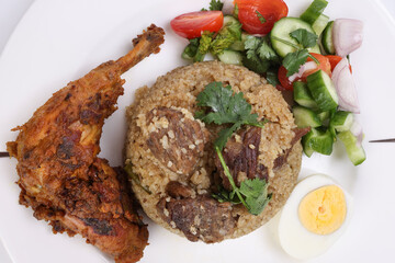 Beef Biryani Tehari with boiled egg coriander leaf garnish chicken curry pot roasted leg tomato cucumber onion chili coriander salad on white plate set over white background