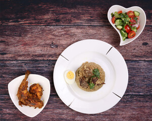 Beef Biryani with boiled egg coriander leaf garnish on white plate chicken curry pot roasted leg triangle dish tomato cucumber onion coriander salad hart shape dish set over rustic wood background