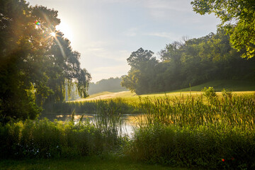 Riverbank on a summer day with a pretty sunrise and green fields