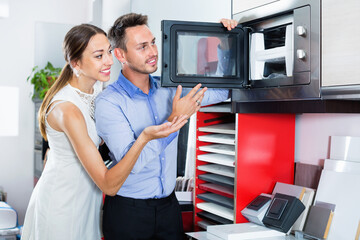 Young positive couple choosing microwave in household appliance section in furnishing store