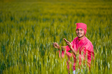 Naklejka na ściany i meble Happy young indian farmer at green wheat field