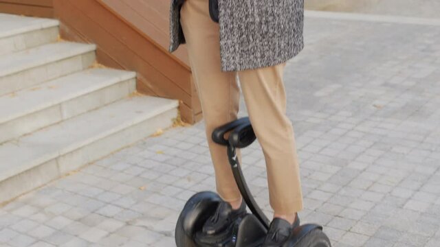 Tilting-up slowmo shot of good-looking business woman working on digital tablet riding gyroscooter outside