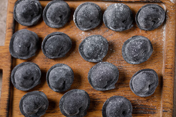 Traditional Russian dumplings, cuttlefish ink ravioli for dough, meat dumplings on a wooden board. View from above.