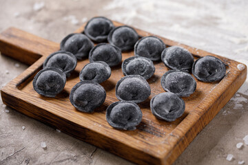 Traditional Russian dumplings, cuttlefish ink ravioli for dough, meat dumplings on a wooden board. View from above.