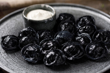 Traditional Russian dumplings, painted with cuttlefish ink for black dough. Still life on a wooden board. Close-up.