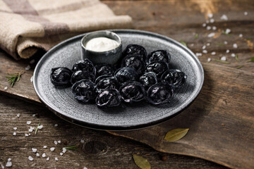 Traditional Russian dumplings, painted with cuttlefish ink for black dough. Still life on a wooden board. Close-up.