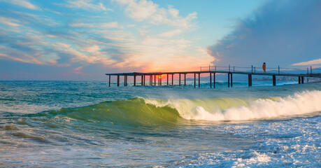 A woman standing on the pier watches the sunset - Long exposure photo of seascape with pier on a sunrise - Alanya, Turkey