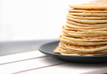 stack of classic pancakes on a black plate on wooden table. pancake week traditional food. crop view. copy space. tasty homemade meal for family brakfast. comforting food.