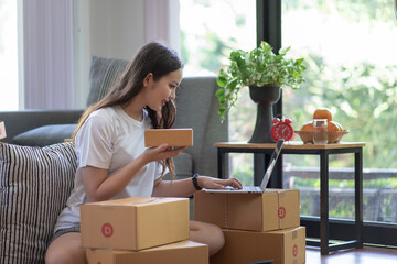 Young Asian woman who owns a small business online  checking order and deliver parcels to customers...