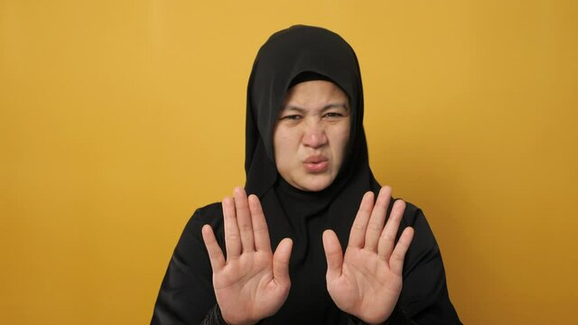 Beautiful Asian musim woman afraid expression with hands raised up, surrender gesture, over yellow background