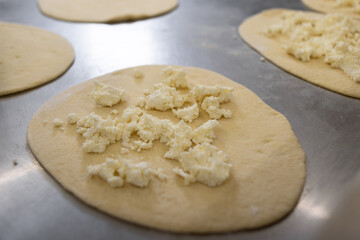 Dough circles for dumplings and pies are rolled out on a metal board, two mugs are filled with cheese. Raw and fresh baked goods.