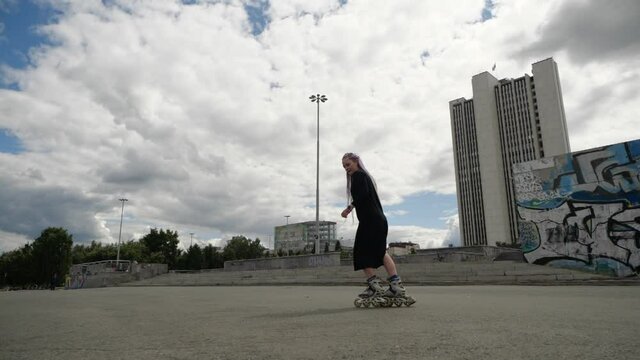 Woman in sports black dress with interesting hairstyle rolls around the city amid graffiti. High quality FullHD footage