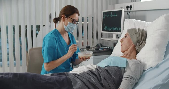 Nurse feeding mature woman having cancer with porridge