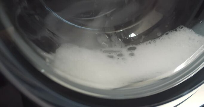 Close up view through glass door of washing machine drum with foam washing clothes
