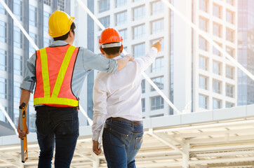 Back view engineer and technician foreman with hardhat helmet working together and viewing building in modern city. Construction, engineering and teamwork concept.