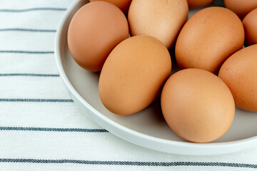 Closeup view of ceramics plate full of many raw whole brown chicken eggs on textile background