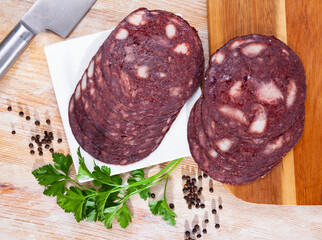 Slices of traditional Spanish blood sausage Botifarra with greens and condiments on wooden surface