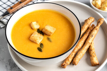 close up of Pumpkin, carrot cream soup in a bowl. with croutons, pumpkin seeds and bread sticks.