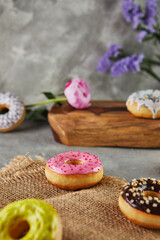 Fototapeta na wymiar Multicolored donuts with glaze and splashes with flowers on a gray background