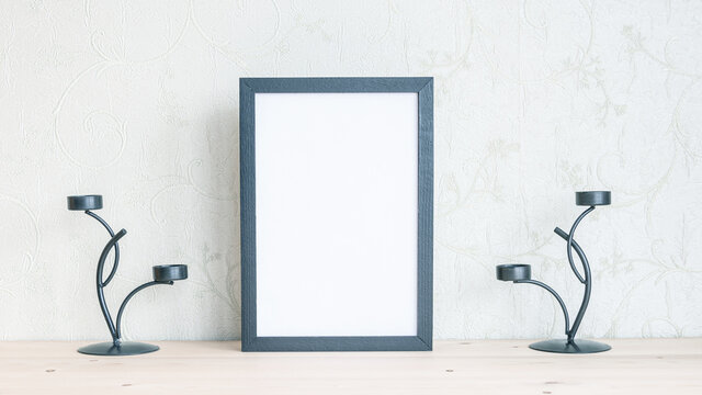 Mockup of a frame for a photo with candle sticks on a wooden table. Vertical.