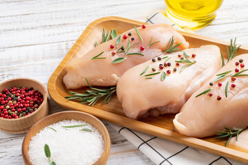 Raw uncooked chicken breasts with spices and herbs on white wooden background, chicken meat with ingredients for cooking.