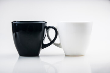Mug mock up. Two ceramic mugs on white background. Blank coffee or tea mugs. Black cup and white cup. Copy space