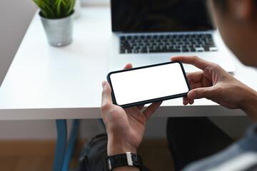 Close up view of young man sitting in office and watching social media in a smart phone.