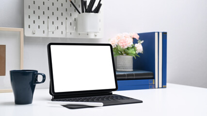 Computer tablet with empty screen, coffee cup and office supplies on white office desk.